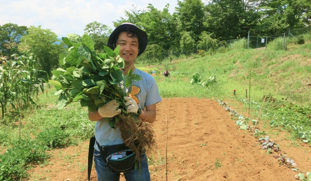 畑で収穫した野菜を持つ務台さんの様子